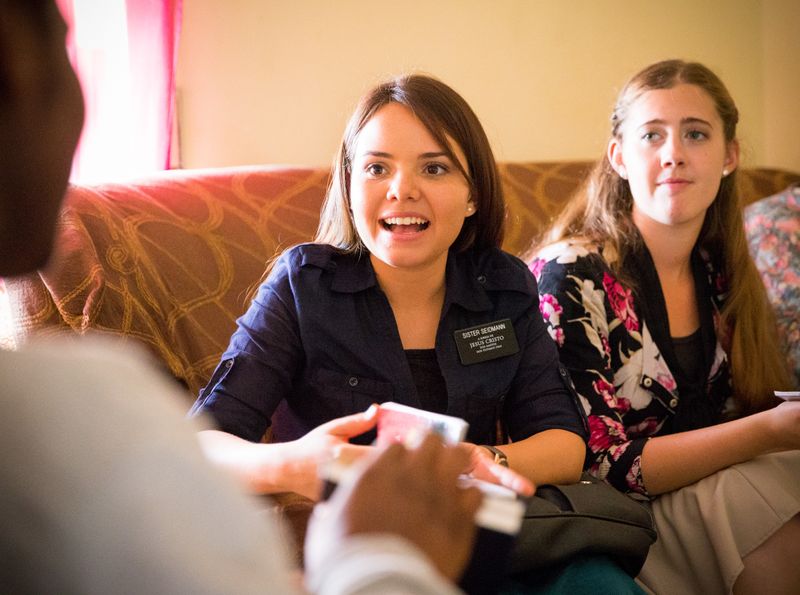 Duas missionárias estudam o Livro de Mórmon com uma mulher no sofá de sua sala de estar