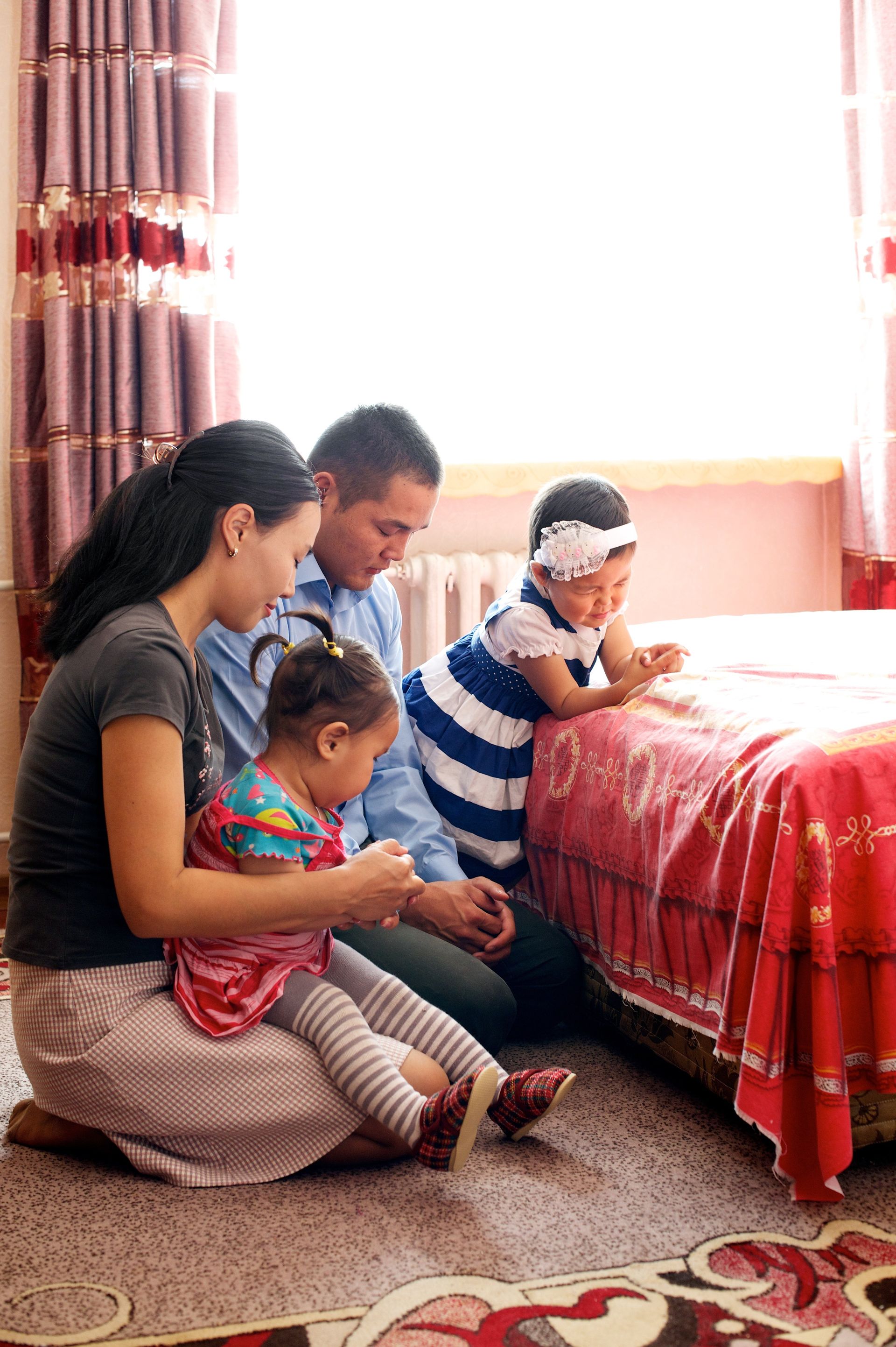 A family kneeling by the bed to pray together.