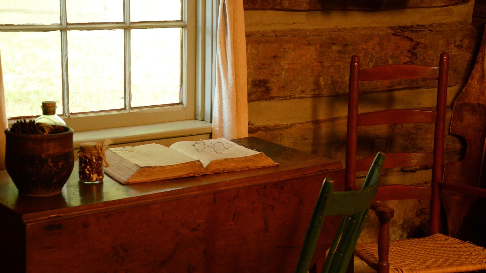 Interior of log home at Peter Whitmer cabin and farm with desk, scriptures, eyeglasses and window.  (horiz)