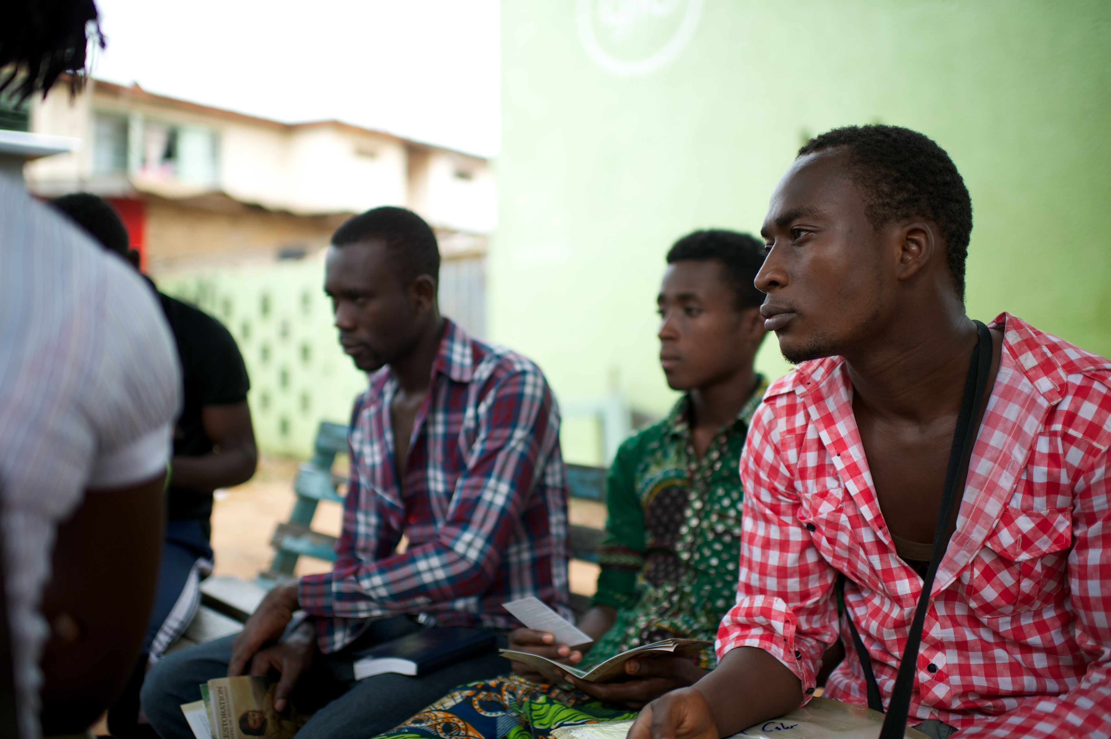 A group of young men in Africa sit on a bench while looking at gospel pamphlets.