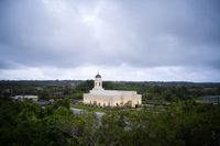 Aerial side view of the Yigo Guam Temple with trees and cloud cover.