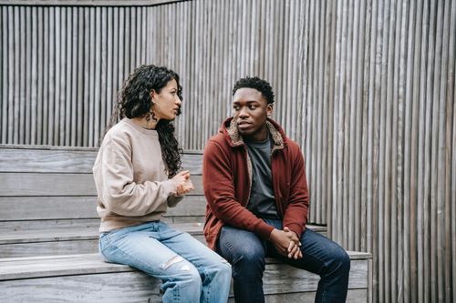 a man and a woman talking while sitting on a wooden bench