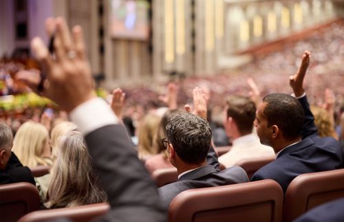 members in the Conference Center raising their hands to sustain leaders