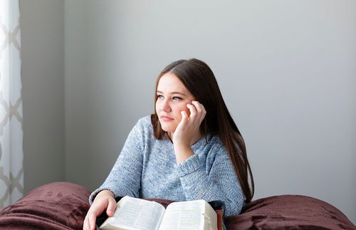 young adult woman pondering while scriptures lie open before her