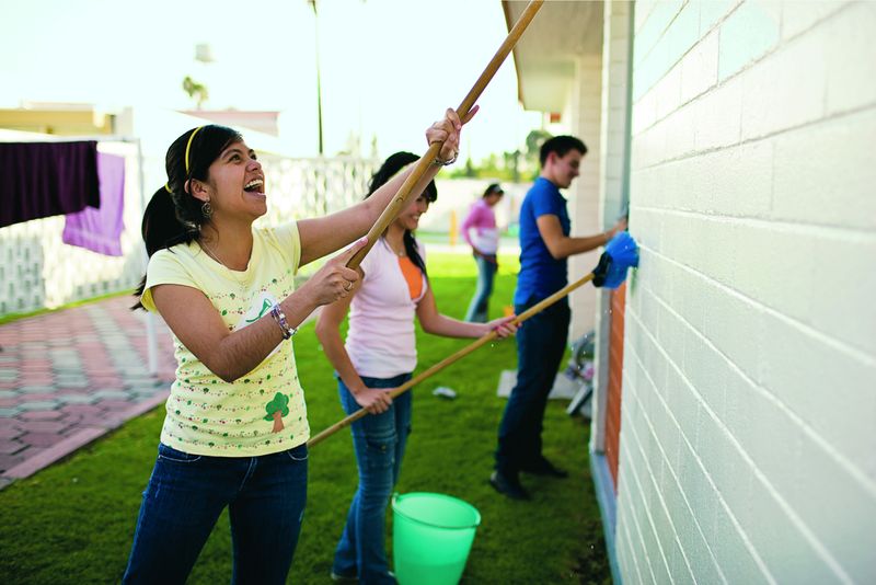 Jovencitas sonrientes y pintando el costado de un edificio