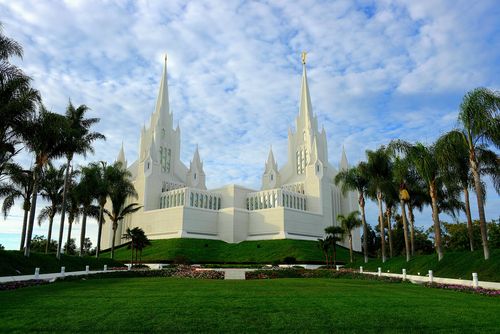 A view of the San Diego California Temple from beyond a large green lawn and rows of palm trees.