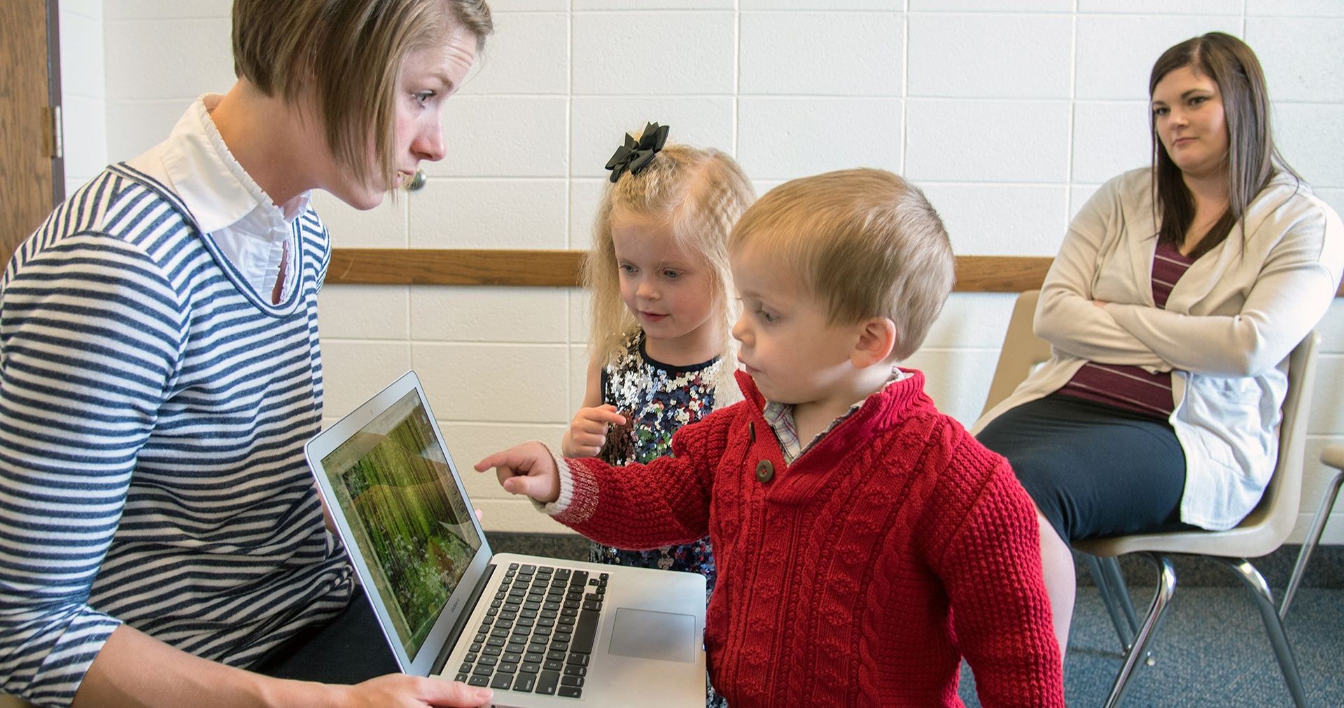 A woman showing a computer to young children.