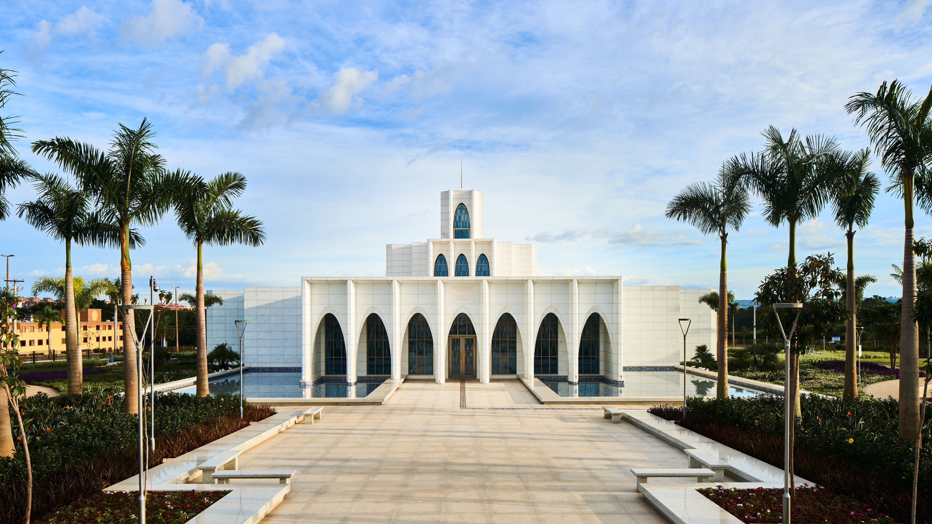 Exterior of the Brasilia Brazil Temple. It features the front of the temple, the entrance area, and trees nearby. Image was taken during the day.