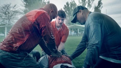 Three men give an injured man a priesthood blessing in the rain on a field