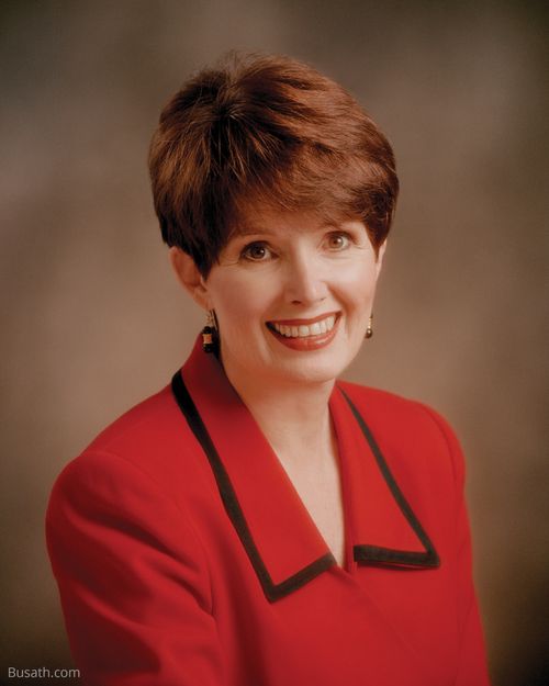 A photograph of Michaelene Packer Grassli against a brown background, wearing a red blazer.