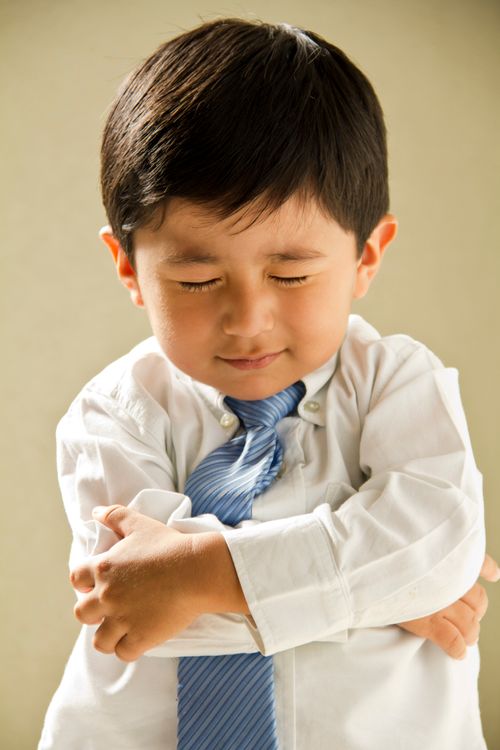 A young dark-haired boy wearing a blue tie folds his arms in prayer.