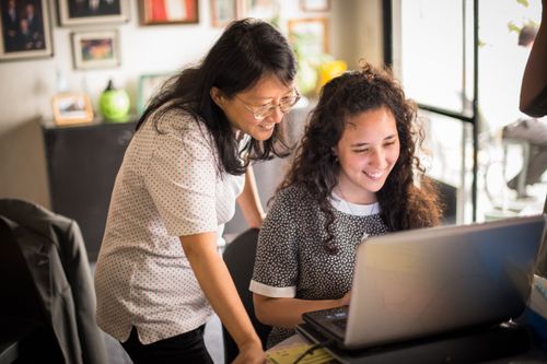 Mother and daughter at a laptop computer in their home.  They are looking at the screen.