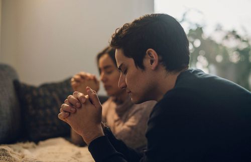 Man and a woman kneeling and praying together at a couch.