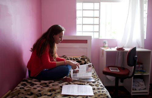 a woman sitting on her bed and reading a magazine