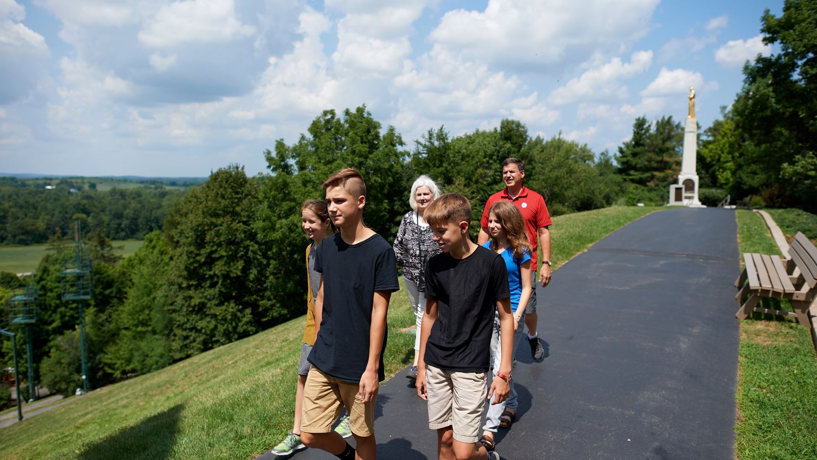 Various family members walk on paved pathways leading to the Hill Cumorah in Manchester, New York.