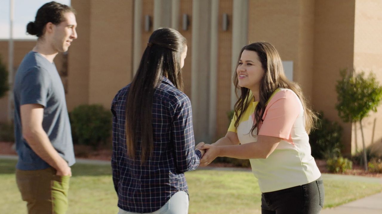 Uma mulher aperta a mão de um casal do lado de fora de uma capela da igreja