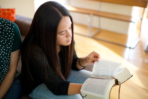 A young woman with dark hair sits next to her mother and reads scriptures.