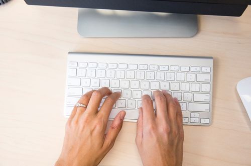 A woman's hands hover over a computer's keyboard. She appears to be typing.