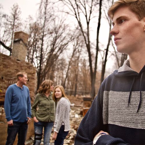 boy standing amid ashes of burned-down home, with family