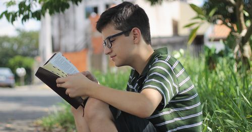 Ein Junge mit einer Brille sitzt draußen und liest in den heiligen Schriften