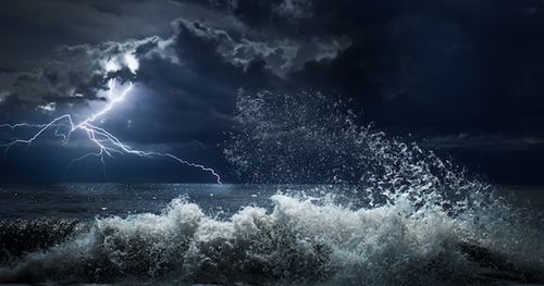 Un océan déchaîné lors d’une tempête avec un éclair qui illumine la nuit.