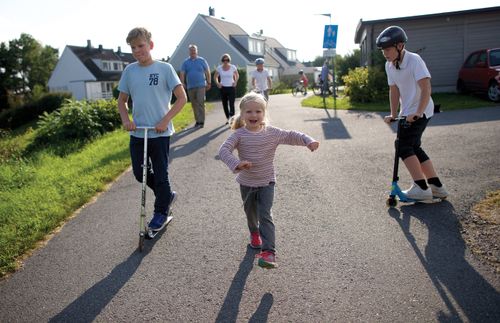 Eine Familie ist zu Fuß unterwegs, zwei Kinder fahren Roller
