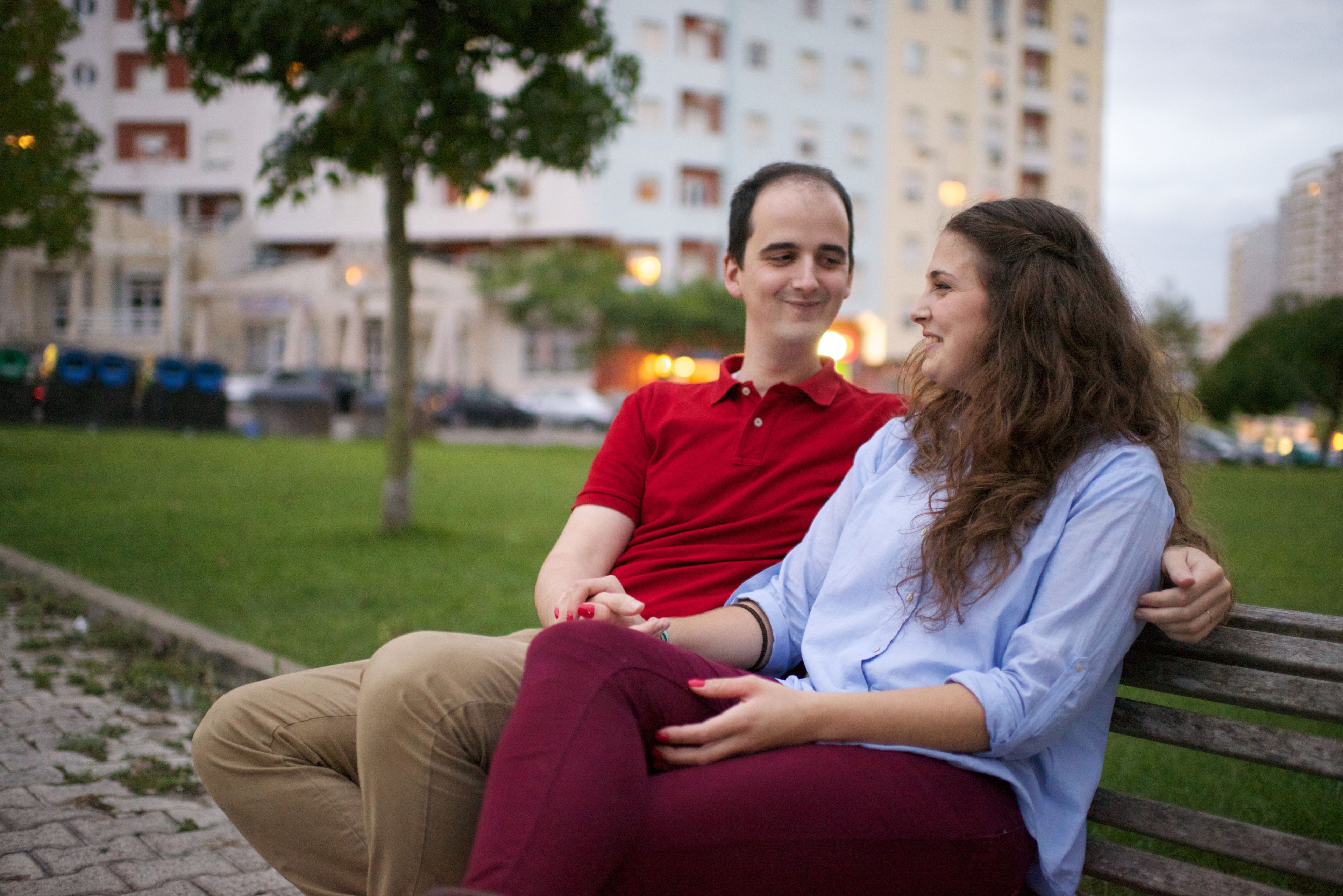 A young couple from Portugal sitting on a wooden bench outside.