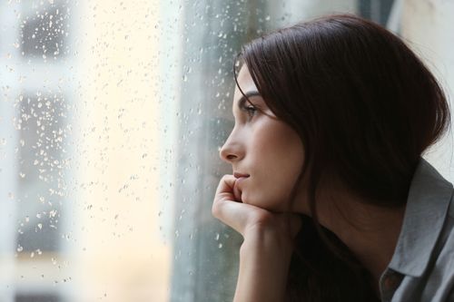 young woman looking out window at rain