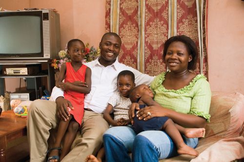 A husband and wife sit on their couch with their young children.
