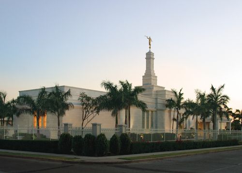 The Hermosillo Sonora Mexico Temple in the evening, surrounded by palm trees and a white fence.