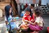 Children are sitting over a pot. they appear to be cutting up vegetables and putting them in a bowl. There are other women sitting near them. This is in Phnom Penh, Cambodia. 

This is part of a stock photography shoot in Cambodia and Hong Kong