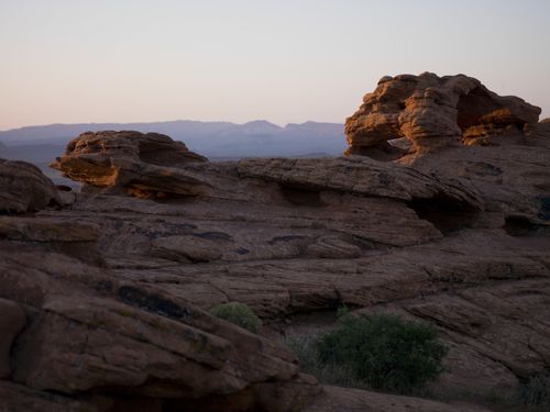 A landscape image of mountains with green brush in the desert at sunset.