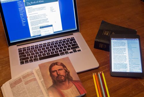 picture of Jesus Christ, physical scriptures, scriptures open on computer and tablet, and colored pencils