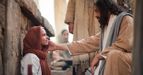 Jesus is touching the cheek of a woman who is sitting on the ground. Outtakes include the ill woman walking up to Jesus to touch his clothes and Jesus kneeling and talking to the seated woman. Jesus touching the face of a seated woman.