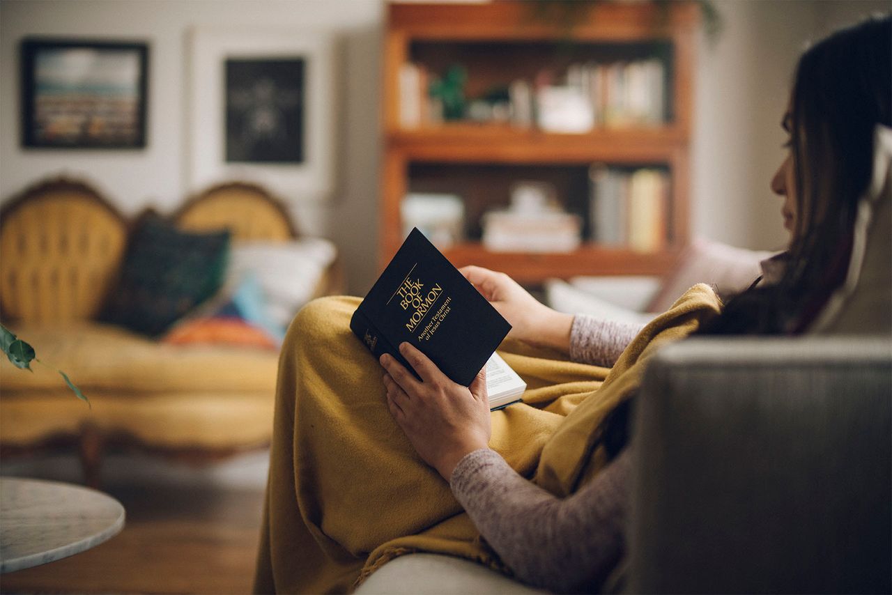A girl reads the Book of Mormon on her couch