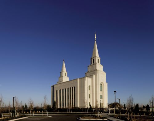 A view of the front and side of the Kansas City Missouri Temple in the daytime, with small trees growing around the parking lot.