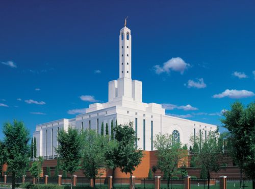 A view from one corner of the Madrid Spain Temple, with green trees growing on the grounds and several small white clouds overhead.