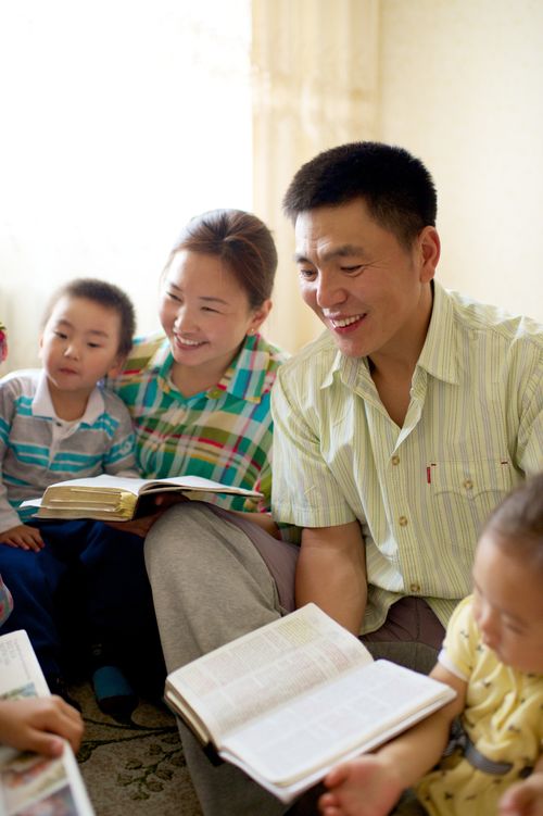 A father sits with his wife and three children on the floor while they read their scriptures together.