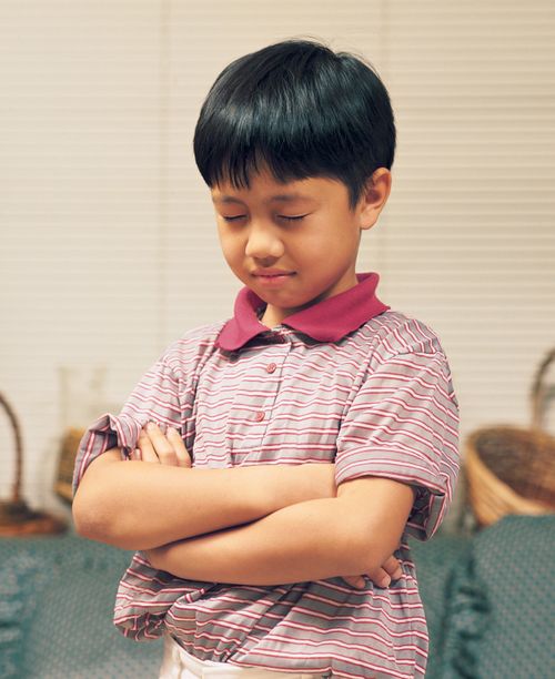 A young boy folds his arms, bows his head, and prays.
