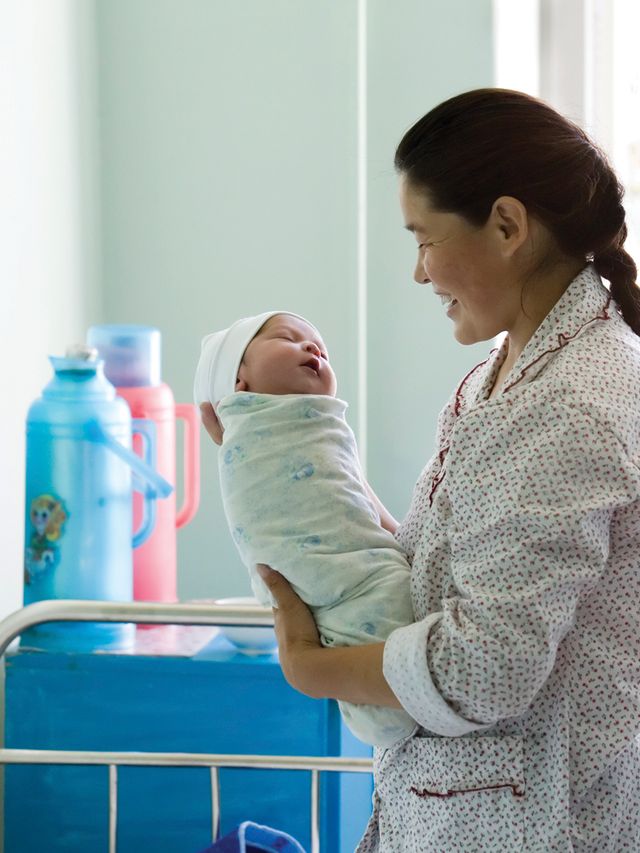 A Mongolian mother standing and holding her newborn baby.