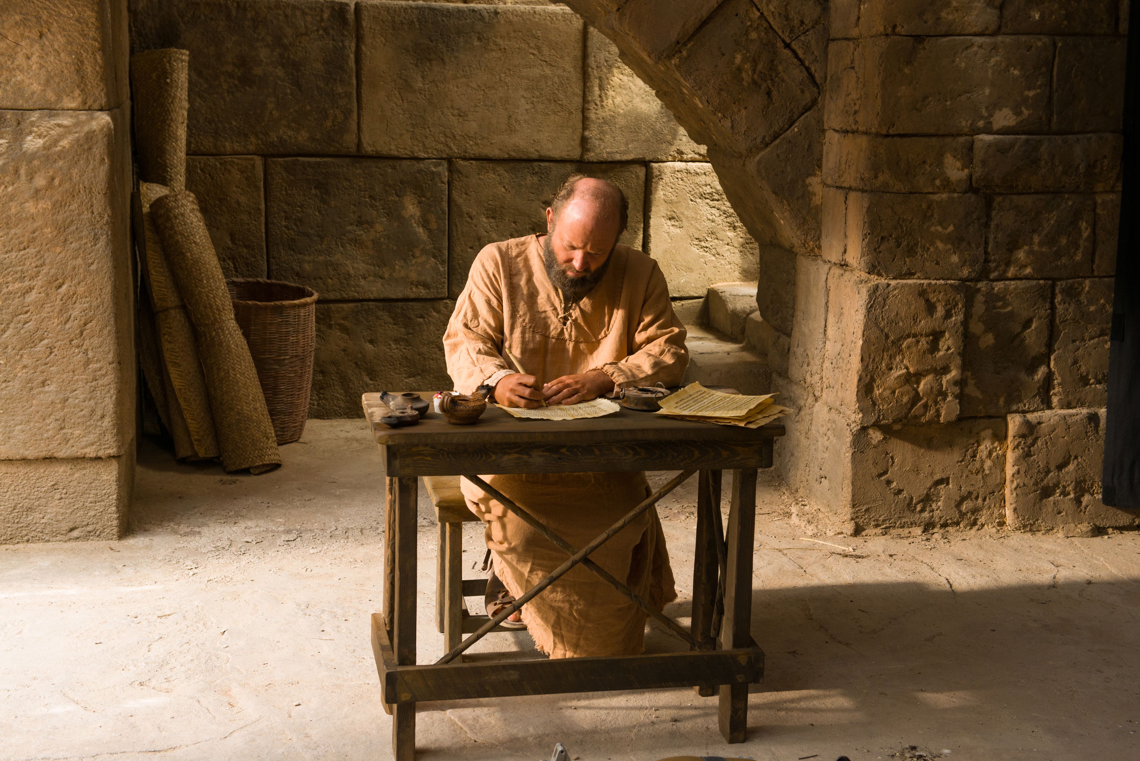 Paul sitting at a table and writing an epistle to the Corinthians.