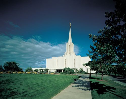 A view of the Jordan River Utah Temple and grounds, with a bright blue sky and one large white cloud overhead.