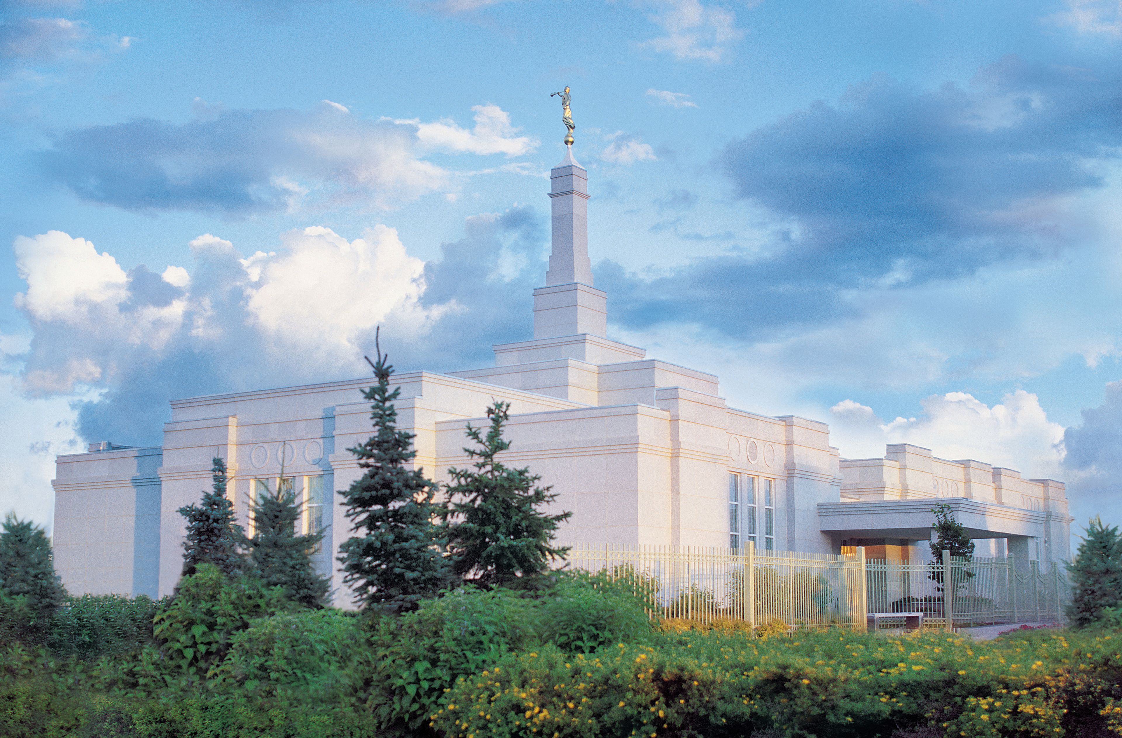 The Regina Saskatchewan Temple, with bushes and evergreen trees growing nearby.