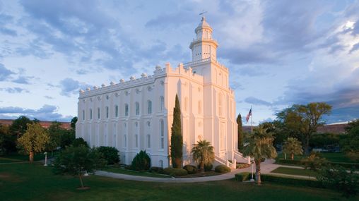 Early morning photograph of the St. George Utah Temple with the sun illuminating the East side of the Temple. Morning clouds whisk through the sky.