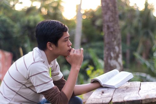 A young man holding scriptures and pondering.