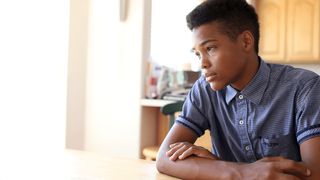 A young black man sitting as he thinks and ponders.  He has a worried or contemplative expression.