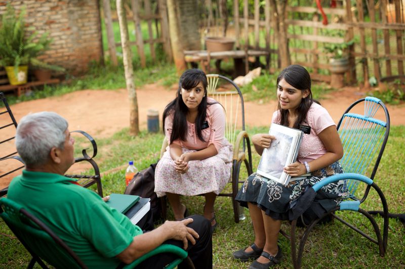Dois missionárias sentadas com um senhor e conversando sobre o Livro de Mórmon e Jesus Cristo