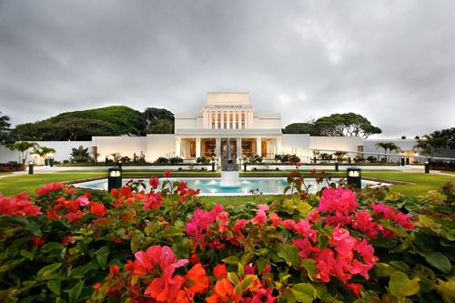 A wide-angle view of the Laie Hawaii Temple, with large pink flowers in the foreground and the temple in the background.