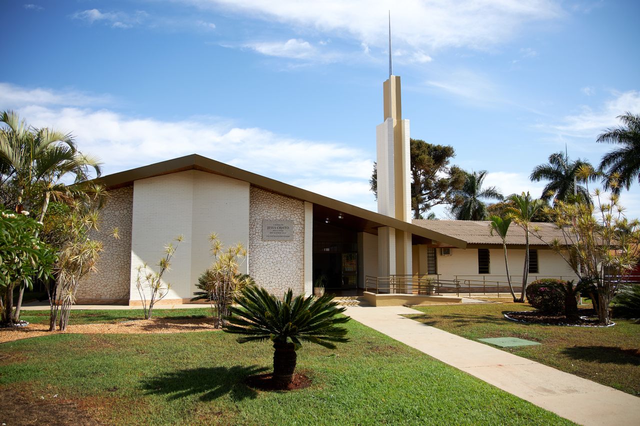 Um homem segura uma porta aberta para uma jovem família entrar na Igreja para aprender sobre Jesus Cristo