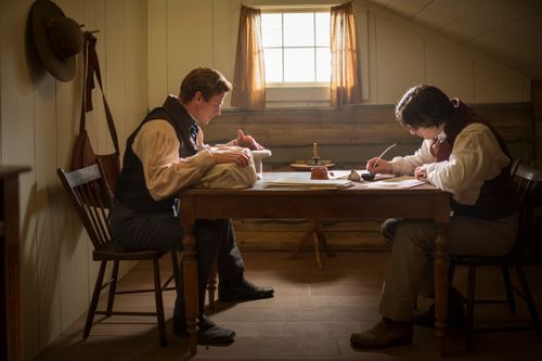 fotograma de una película histórica: José y Oliver sentados uno frente al otro en una mesa, Oliver escribiendo